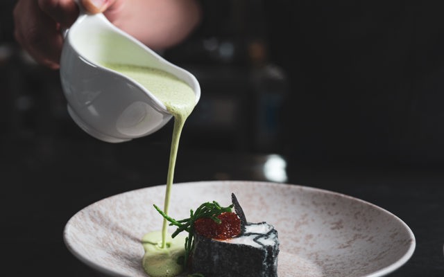 En servitör häller grön sås på en tallrik med mat