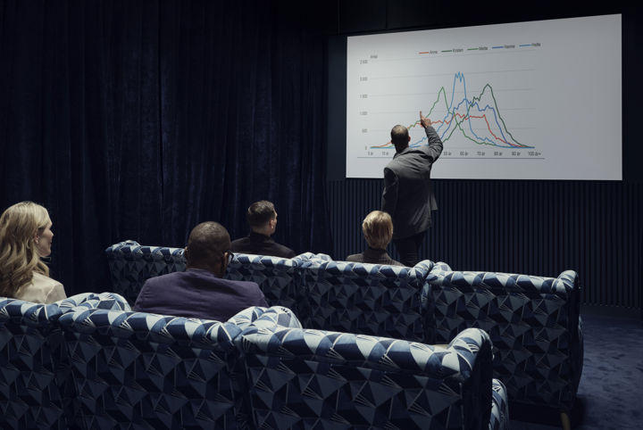 Människor sitter i soffor och lyssnar på en föreläsning i ett konferensrum