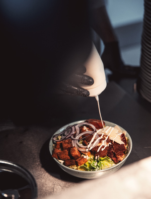 En person häller på dressing på en sallad