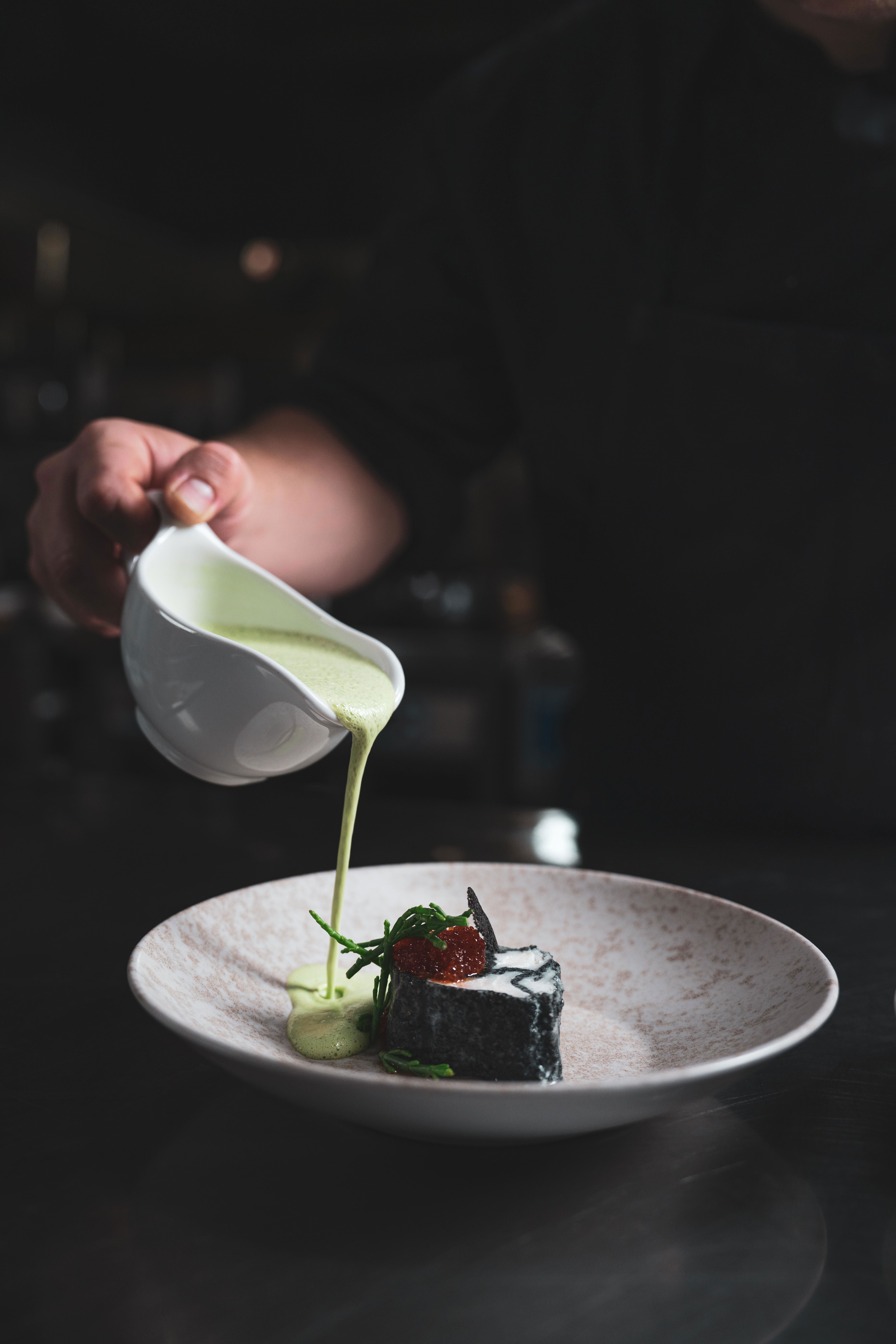 En servitör häller grön sås på en tallrik med mat