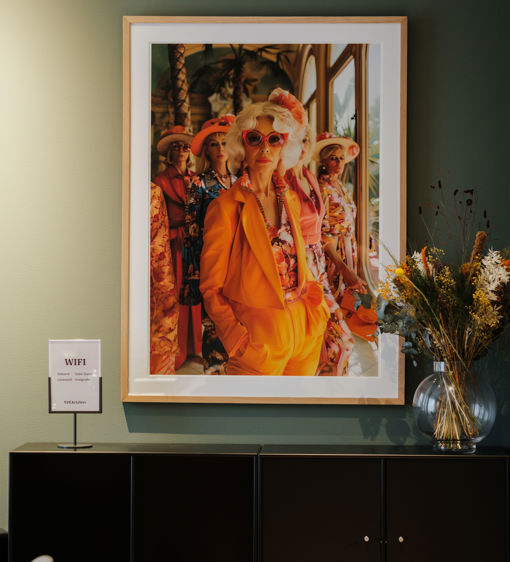 PÅ väggen hänger en tavla som föreställer en kvinna i orange kostym och röda solglasögon
