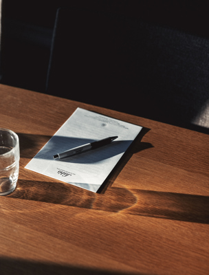 Ett anteckningsblock och penna ligger på ett träbord