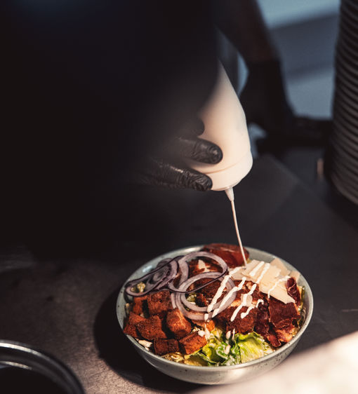 En person häller på dressing på en sallad