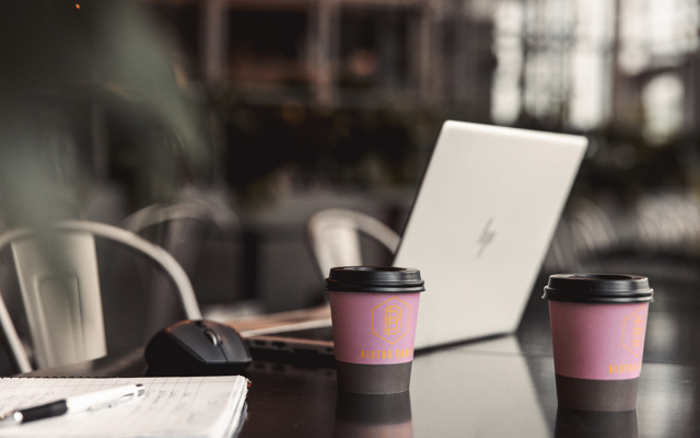 Två to-go-muggar och en laptop på ett bord